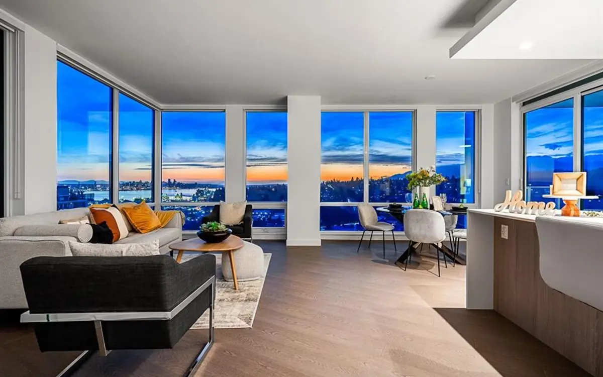 High-floor living and dining room at dusk with wraparound windows over the city and inlet