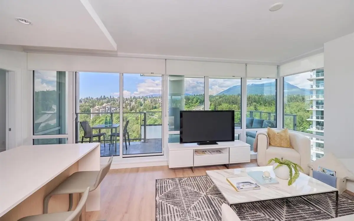 Corner living room opening onto a balcony with mountain and treetop views