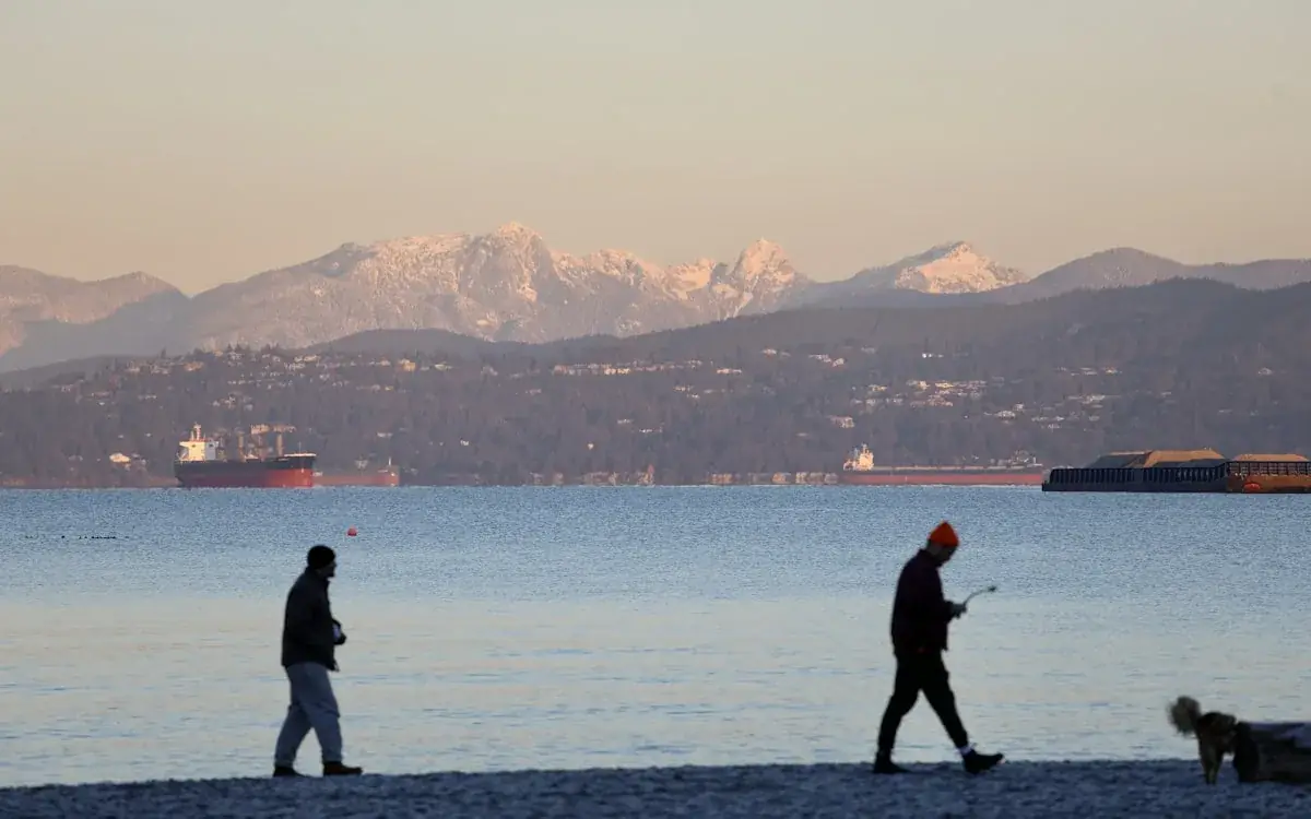 Walkers on a Vancouver beach with snow-capped North Shore mountains beyond