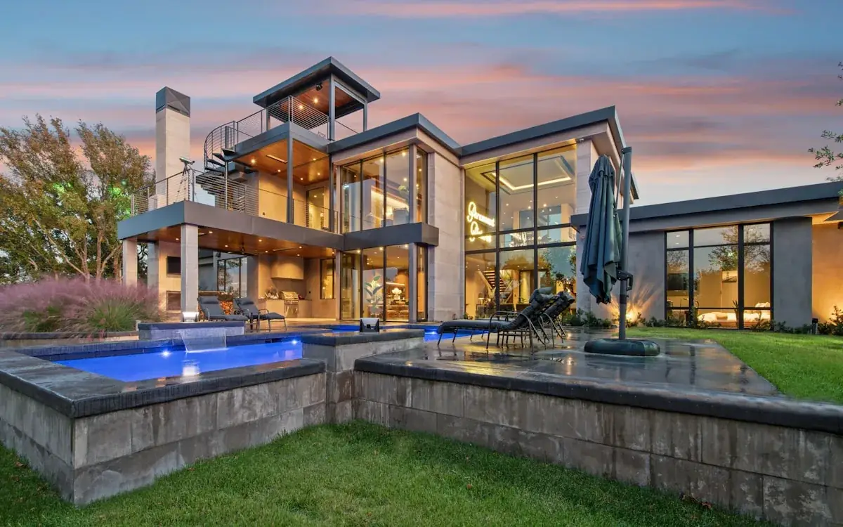 Modern luxury home with pool and glass walls glowing at dusk
