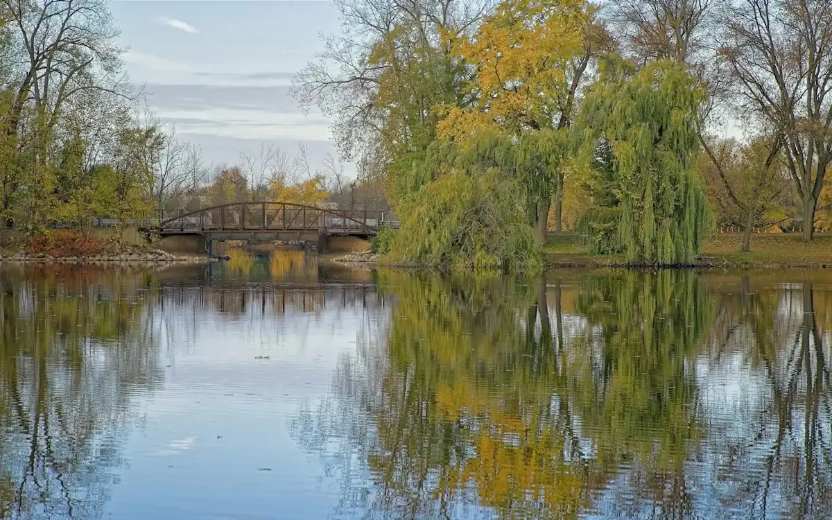Calm park lake with a footbridge and autumn trees reflected