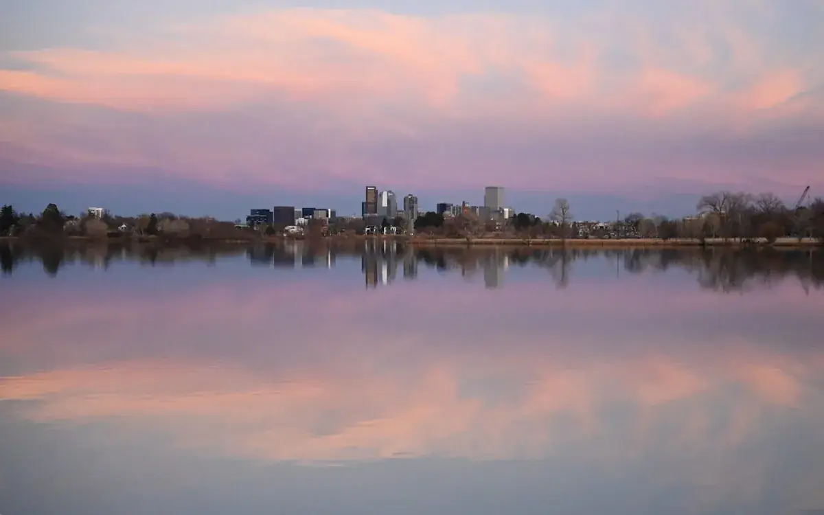 City towers reflected in a still lake under a pink sunset sky