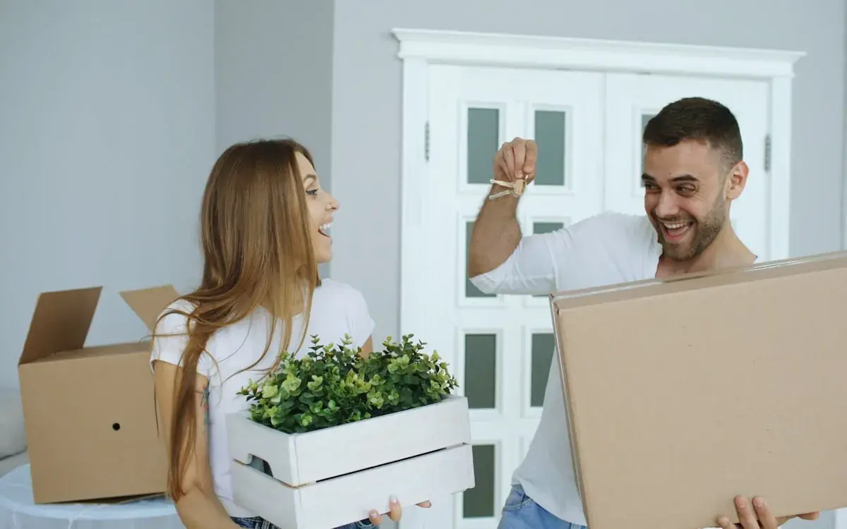 Happy couple carrying moving boxes and holding the keys to their new home
